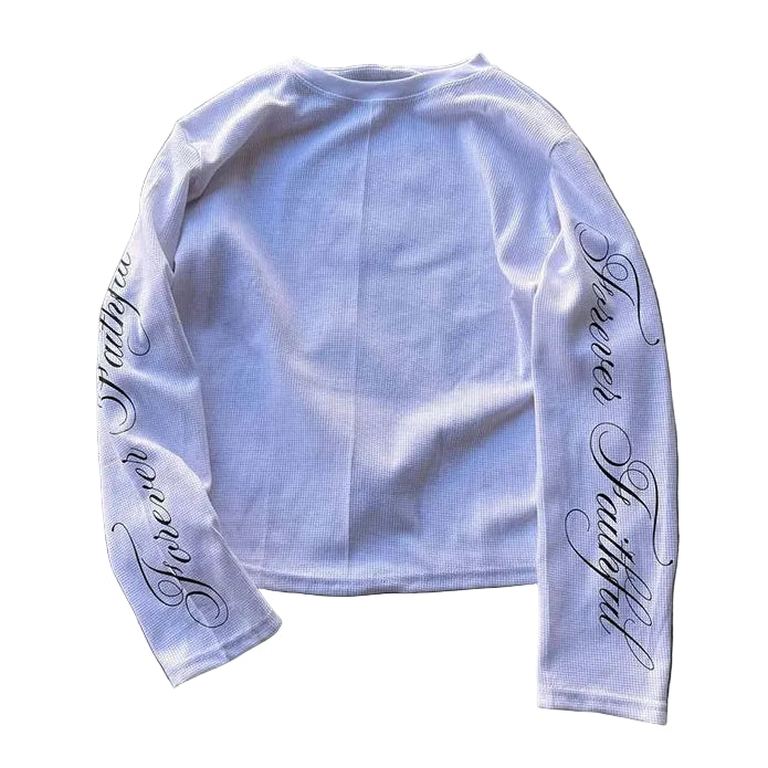 White long-sleeve shirt with cursive text on sleeves against a gray concrete background